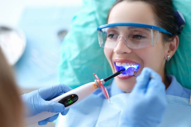 Dentist works with dental polymerization lamp in oral cavity. Caries treatment concept