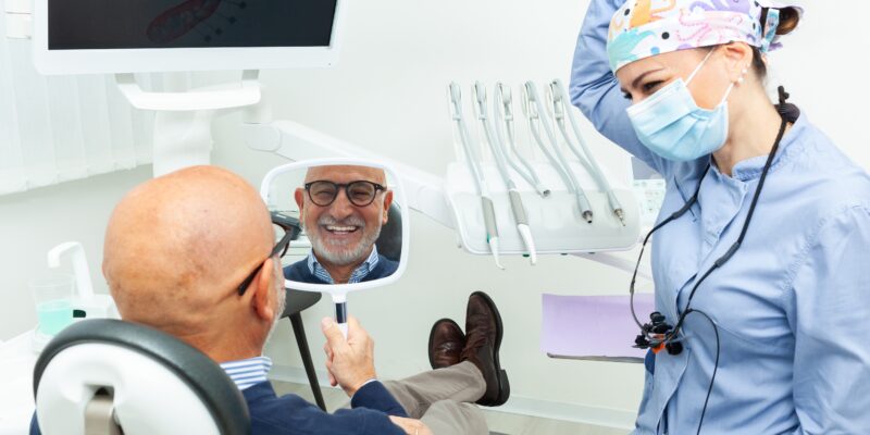 man smiling in a mirror looking at his new dentures in Los Angeles