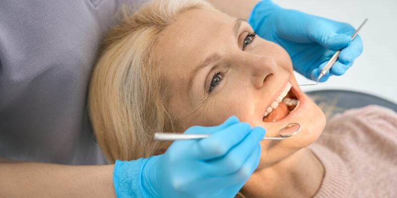dentist in blue gloves inspecting a female patients dental crown