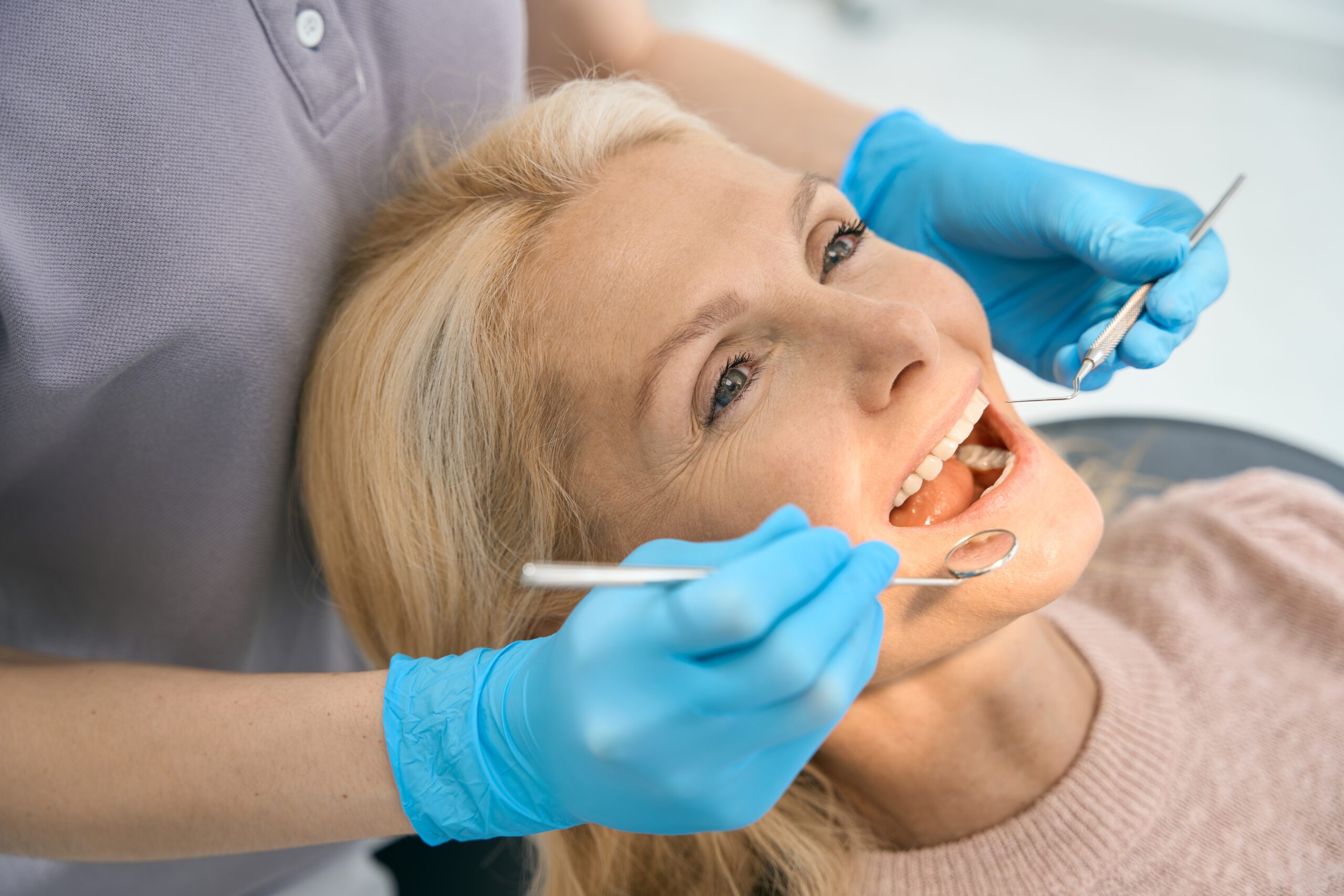 dentist in blue gloves inspecting a female patients dental crown