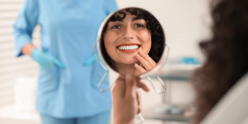 woman smiling in mirror, happy with newly bonded teeth