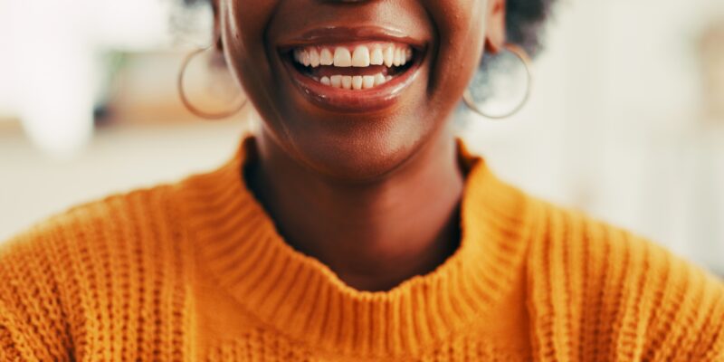 closeup of woman in an orange sweater, perfect white smile