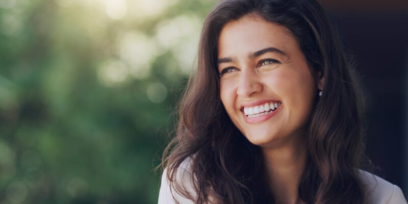 young woman outdoors in nature showing her perfect white smile