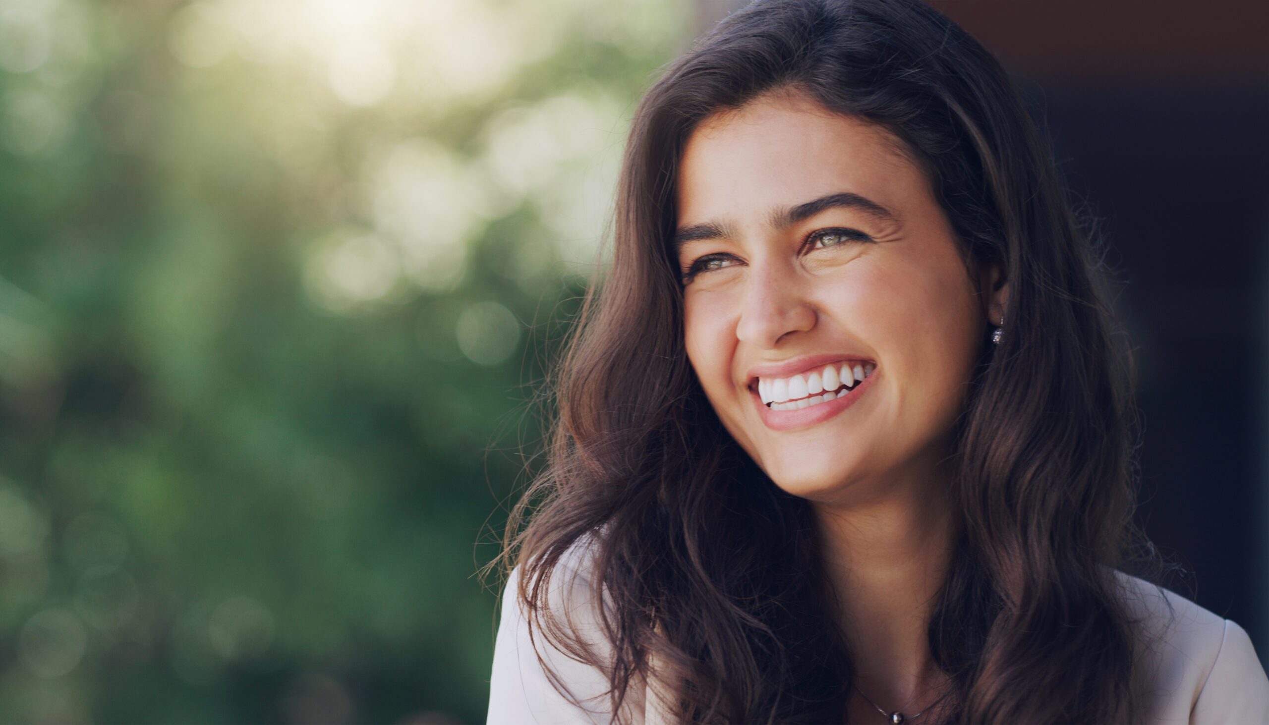 young woman outdoors in nature showing her perfect white smile